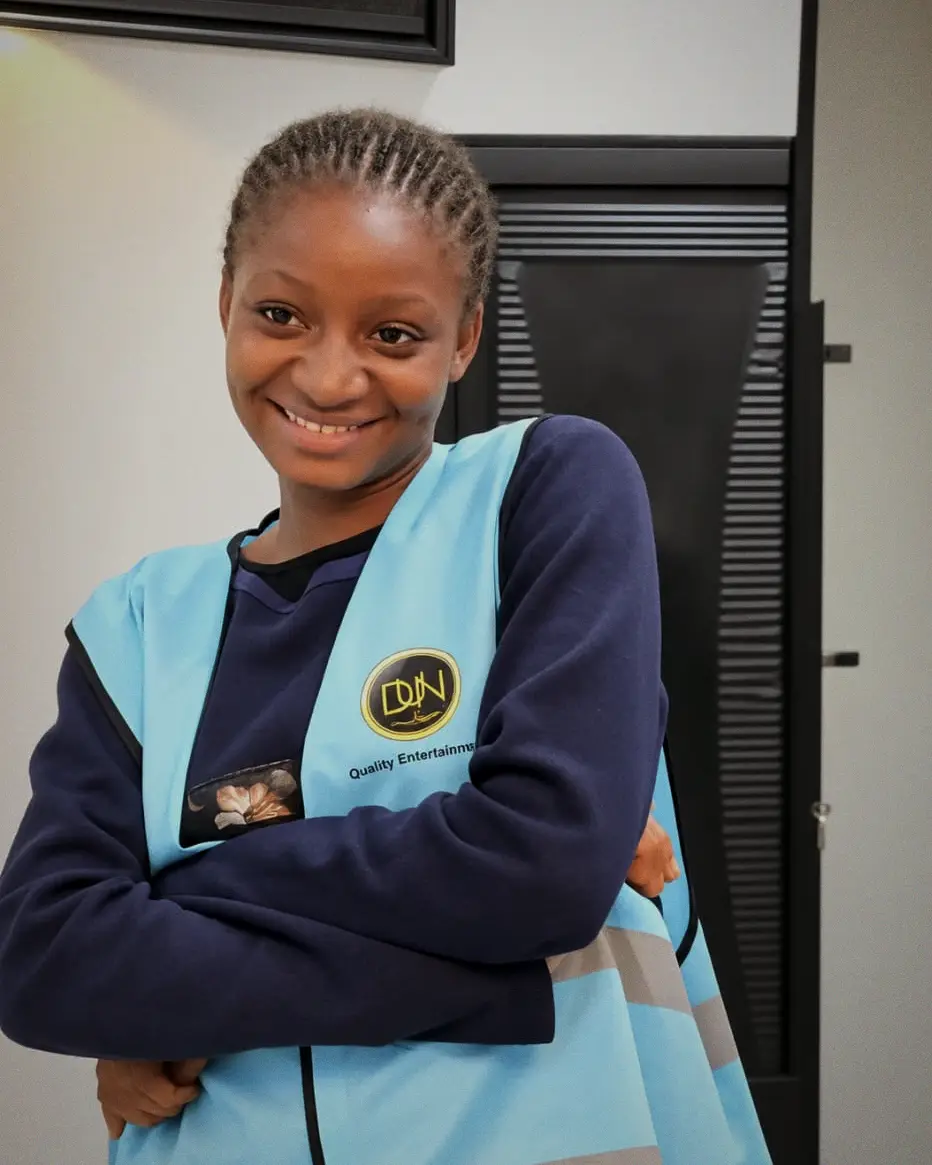 A young crew member in a light blue DUN vest stands with arms folded, smiling.